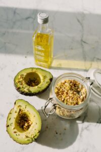 Fresh avocado halves with pine nuts and olive oil on marble surface, highlighting healthy eating.